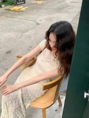 Woman wearing an ivory floral lace maxi dress and spaghetti strap slip dress set with a fitted floor length silhouette, straw tote bag, and gold ring outdoors
