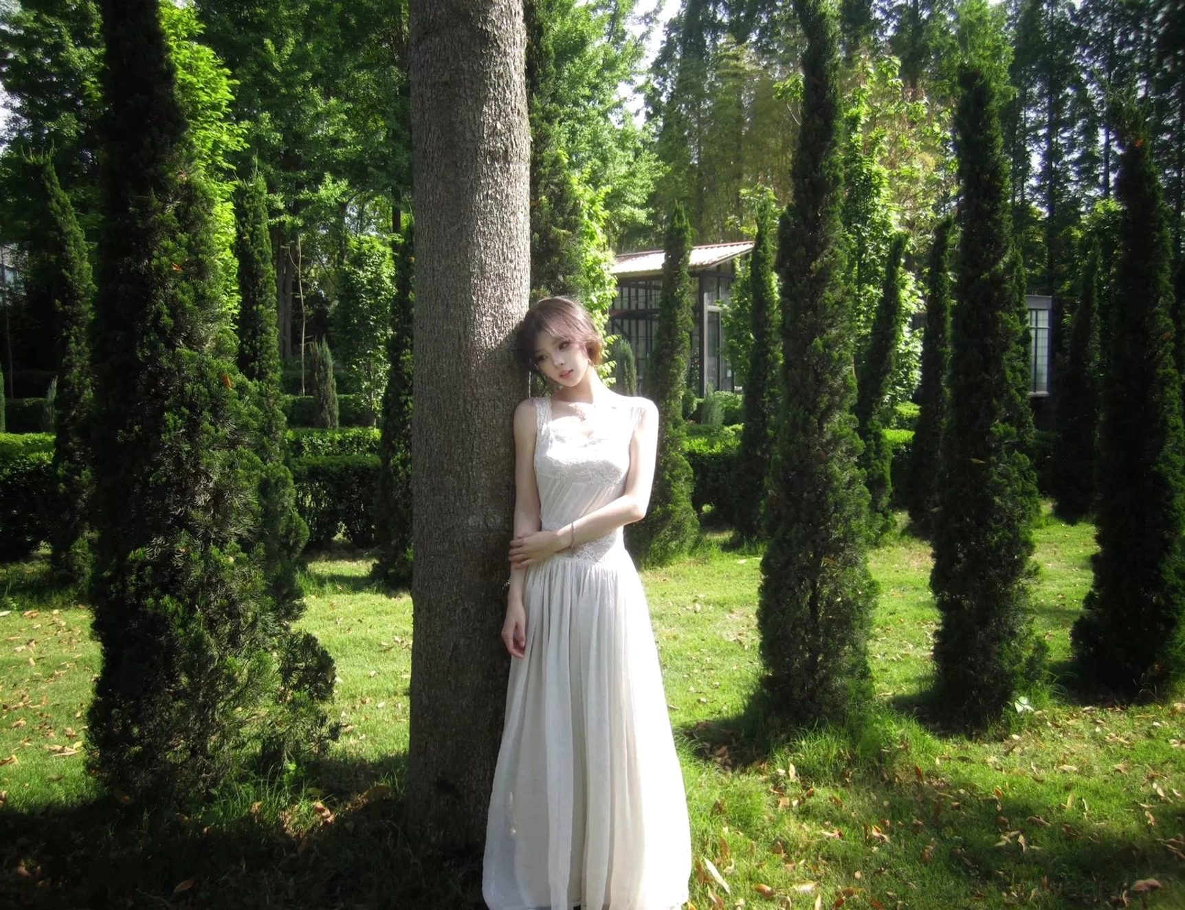 Front view of an ivory lace open-back maxi dress with a fitted bodice, sleeveless design, round neckline, and flowing floor-length A-line skirt in an outdoor garden
