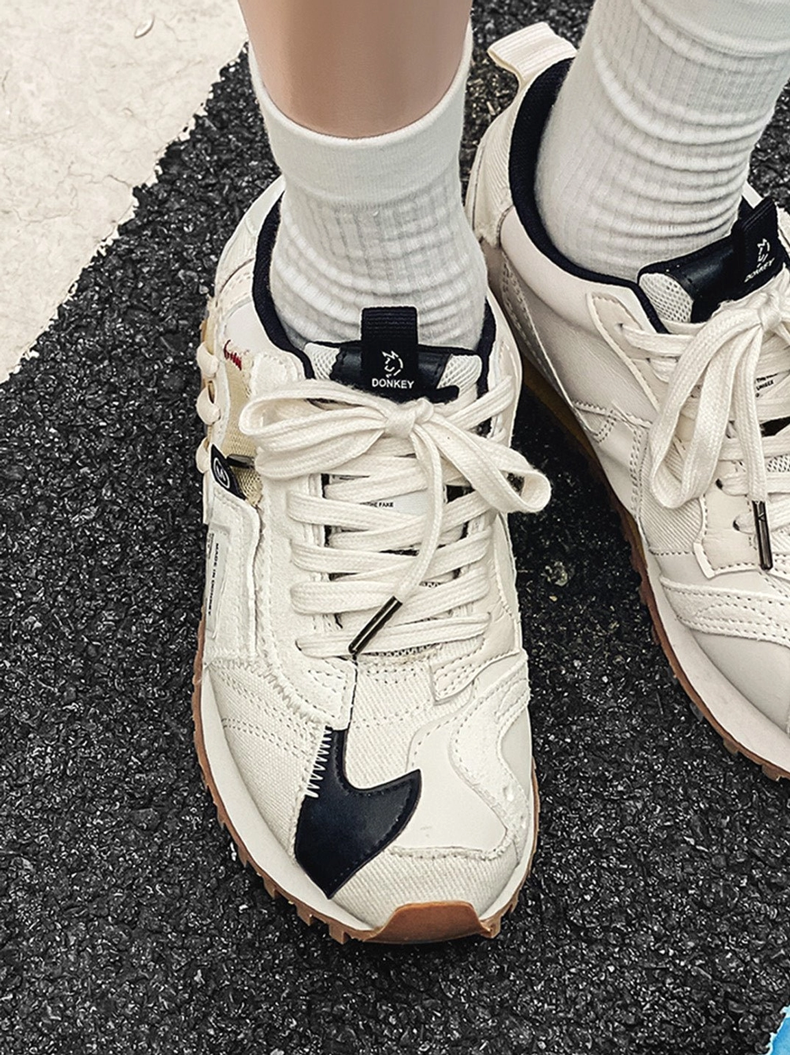 Front overhead view of ivory lace-up retro runner sneakers worn on feet with black decorative accents and gum waffle soles
