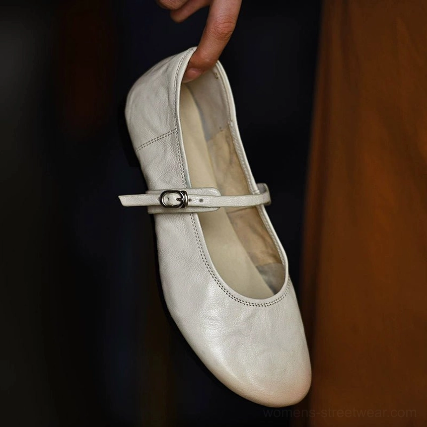 Angled handheld view of an ivory lambskin Mary Jane flat featuring a soft leather texture, adjustable slim strap, silver buckle, and low heel