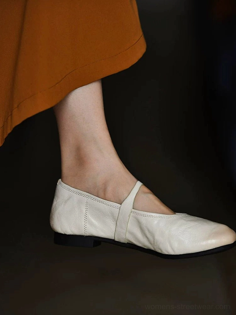 Ivory lambskin Mary Jane flat shoe worn with a caramel maxi skirt, showing the rounded toe, slim buckle strap, and low rubber heel in side view