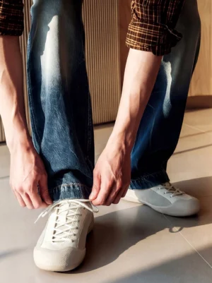 White gray ivory mesh-panel canvas low-top sneakers worn with jeans while tying laces indoors