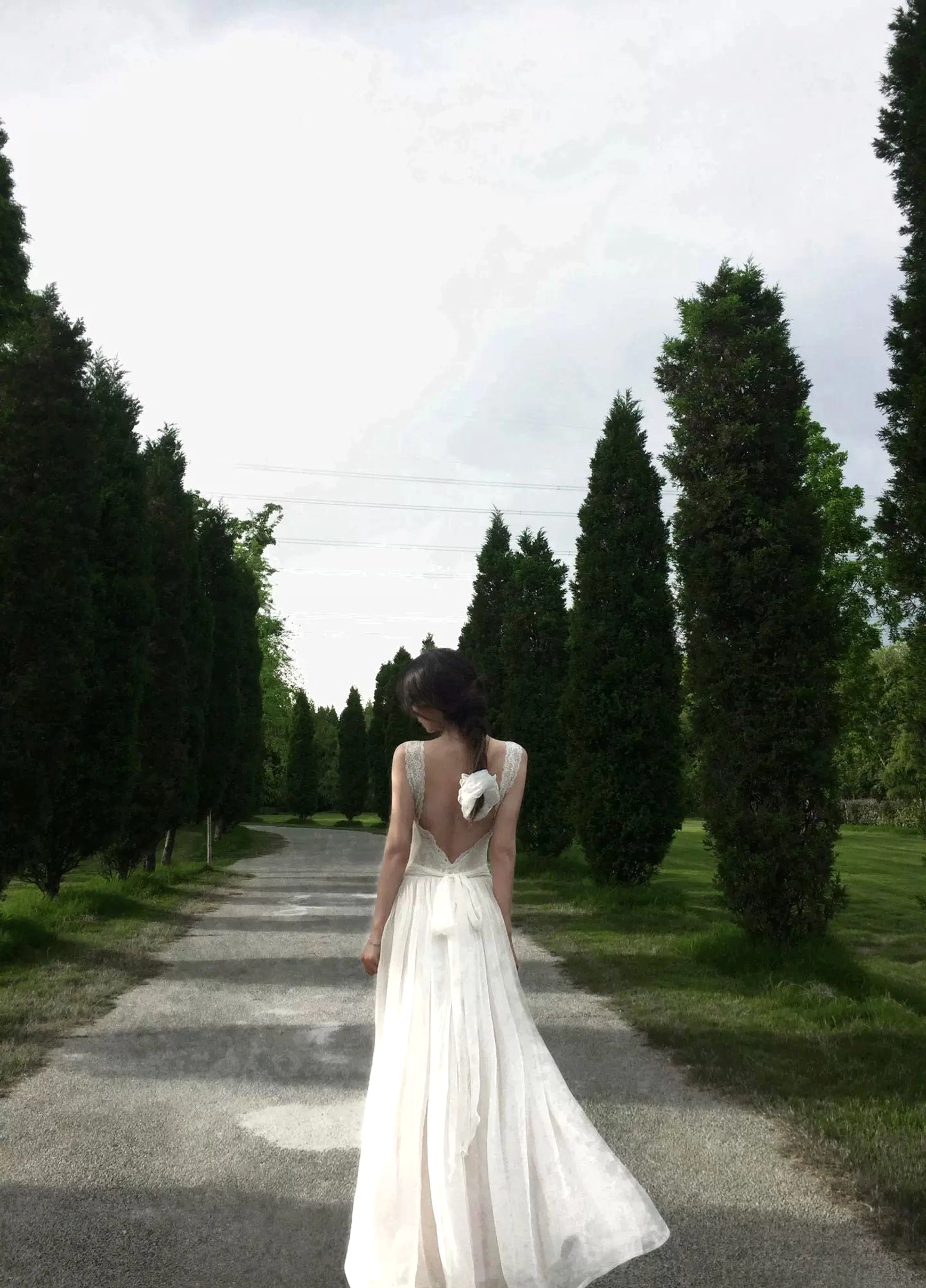 Back view of an ivory open-back maxi dress showing the deep V back, adjustable waist ties, bow detail, and softly flowing chiffon-style full-length skirt