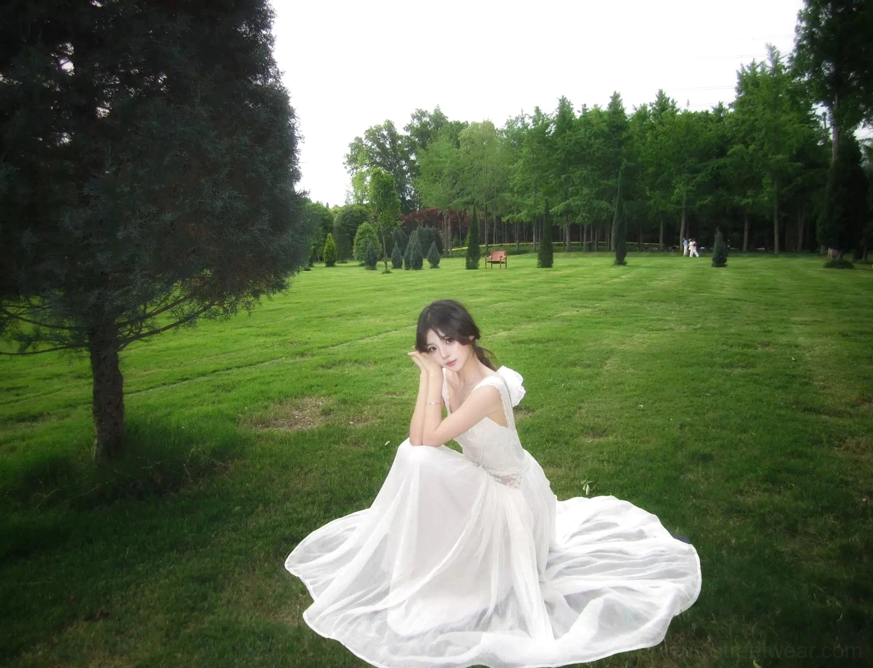 Side seated view of an ivory open-back maxi dress with a back bow, sleeveless silhouette, flowing train effect, and elegant outdoor occasionwear styling