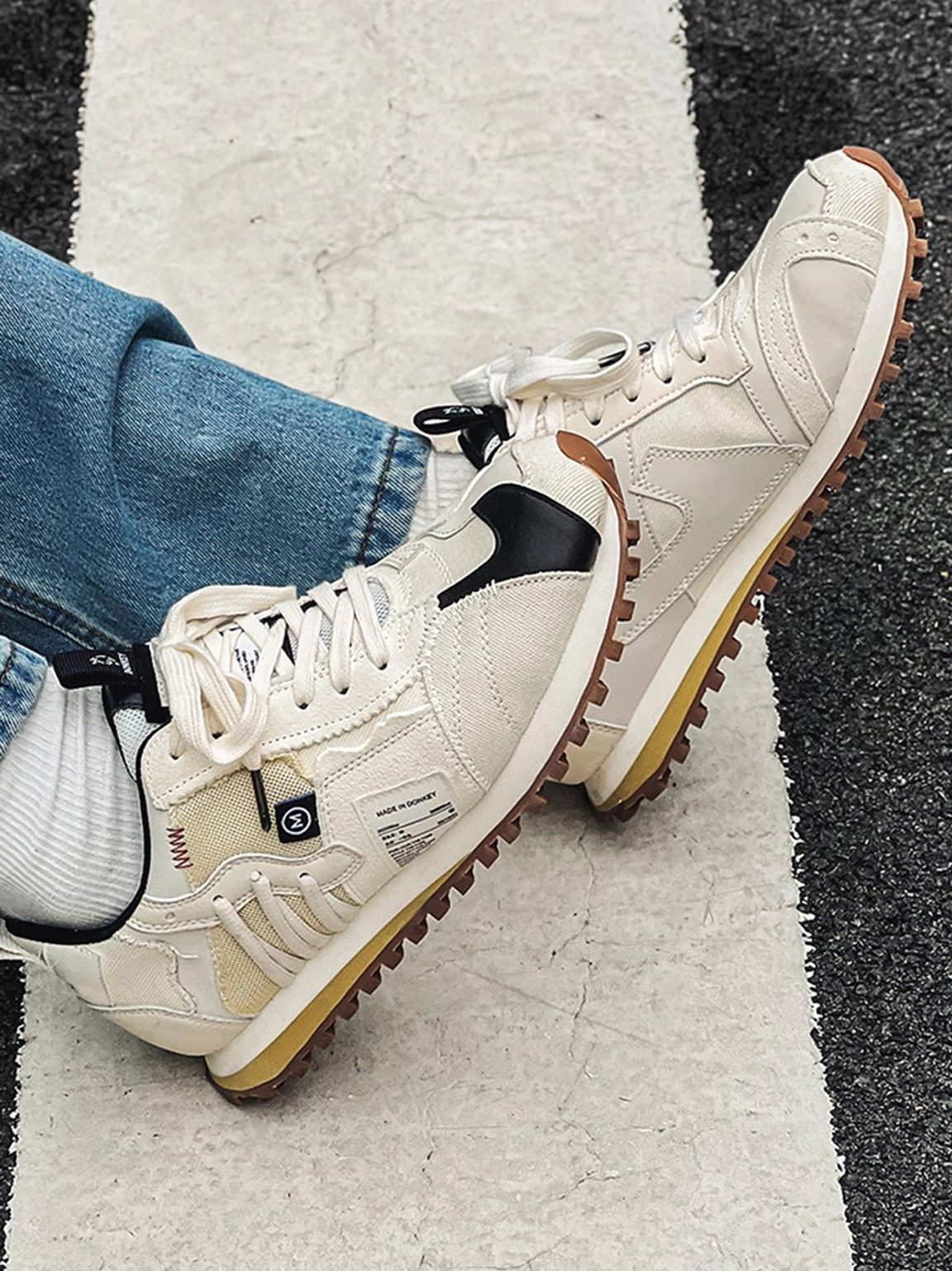 Ivory retro running sneakers with exposed decorative stitching, black toe caps, and yellow brown gum soles styled with blue denim