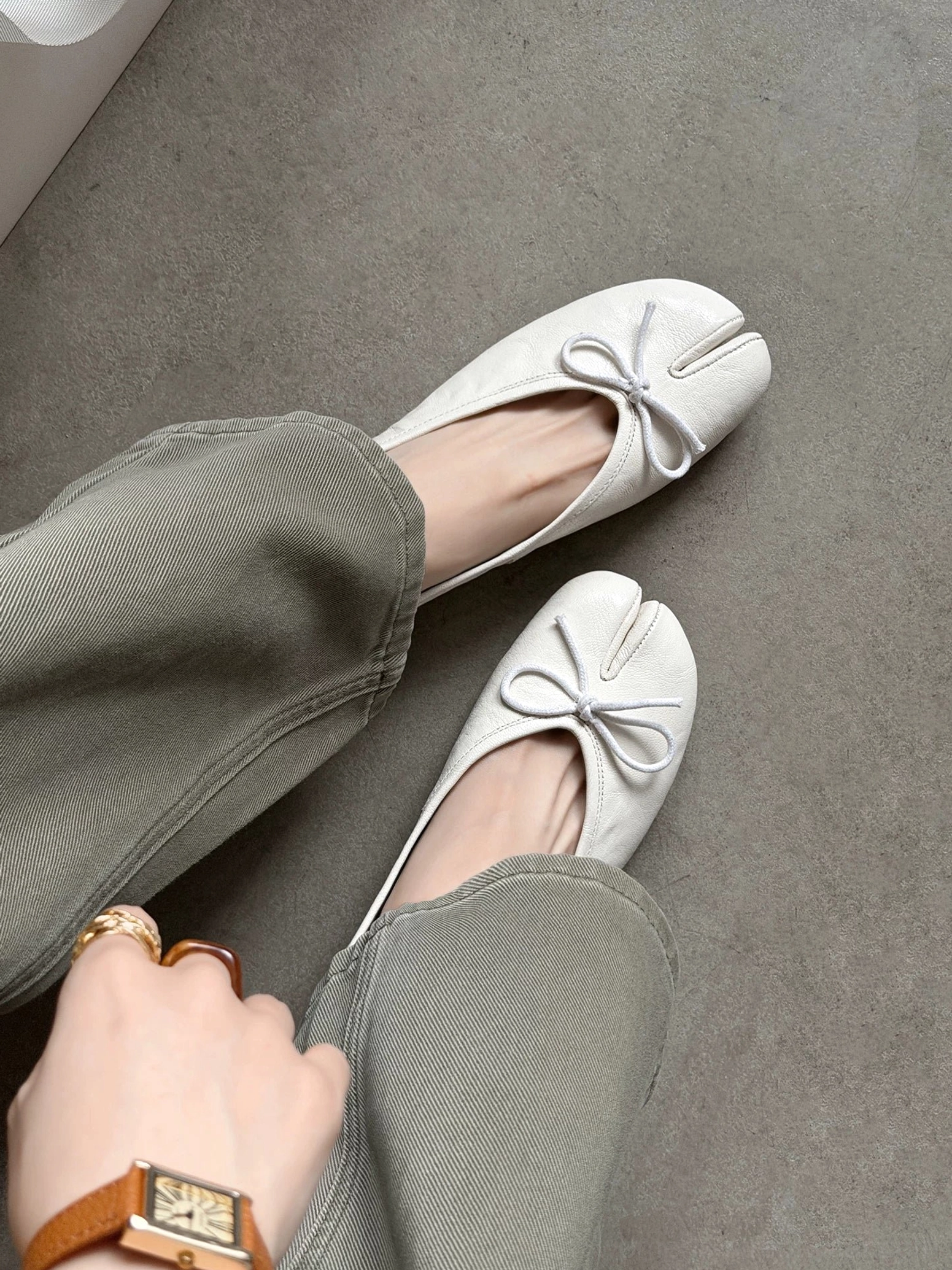 Ivory split-toe leather ballet flats with gathered bow detail worn with grey jeans in close-up view