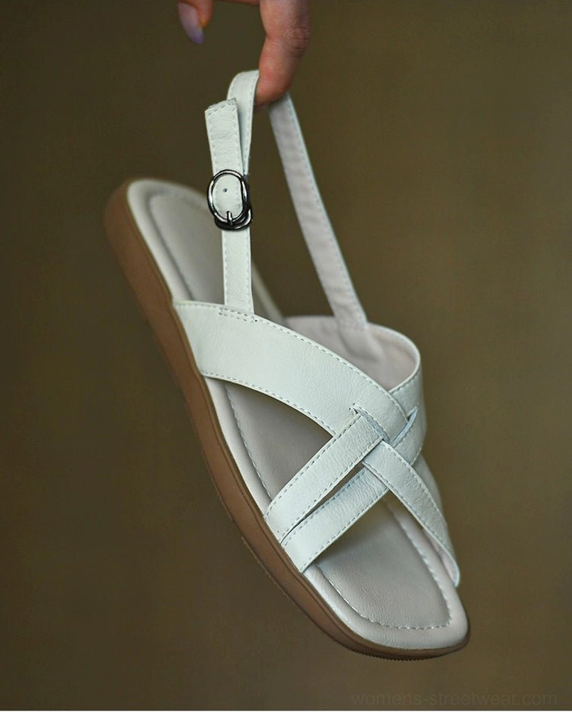 Side angle of ivory leather cross-strap flat sandals showing the adjustable slingback buckle, soft padded insole, and low tan outsole