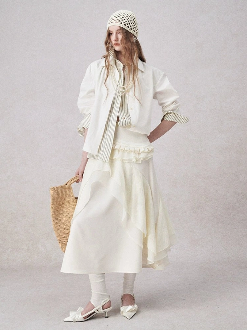 Woman wearing an ivory striped contrast-collar cotton blend shirt layered with a ruffled midi skirt, knit hat, straw tote, and bow pointed heels in a minimalist streetwear outfit
