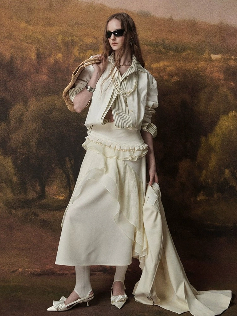 Full-body Korean streetwear styling of a relaxed ivory striped contrast-collar shirt with rolled cuffs, ruffled midi skirt, black sunglasses, and straw shoulder bag