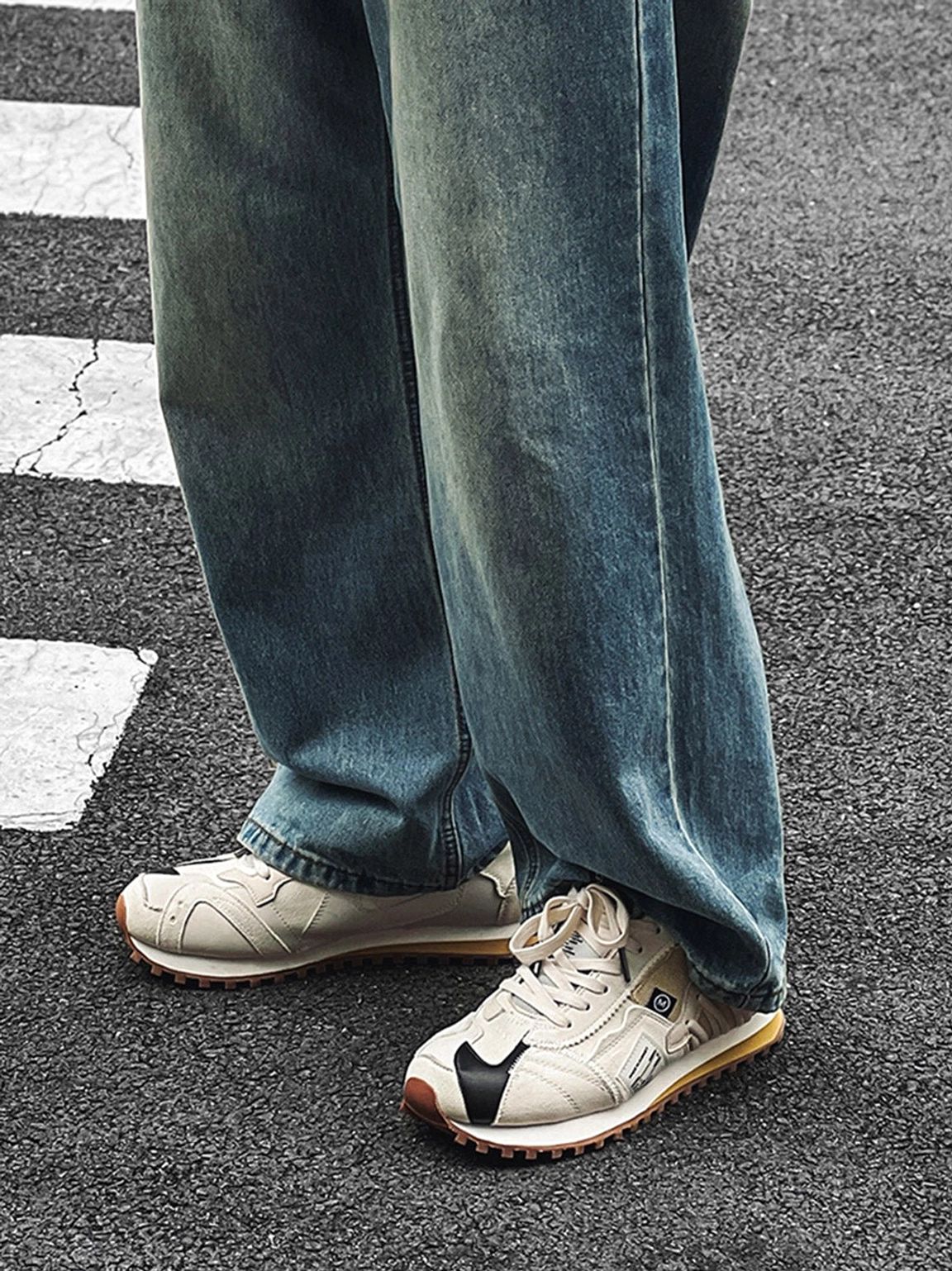 Ivory unisex retro runner sneakers with black toe accents and brown waffle soles worn with loose blue jeans on an urban road