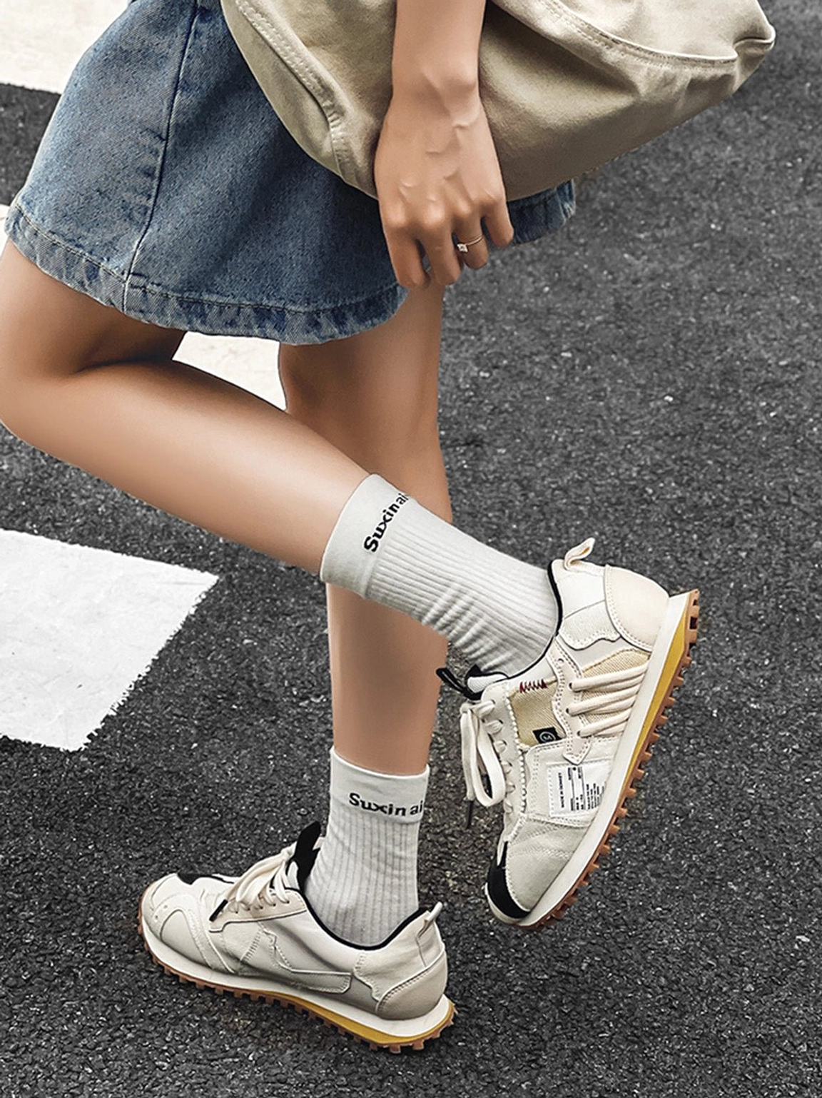 Ivory waffle sole retro runner sneakers worn with a denim skirt and white crew socks on a city zebra crossing