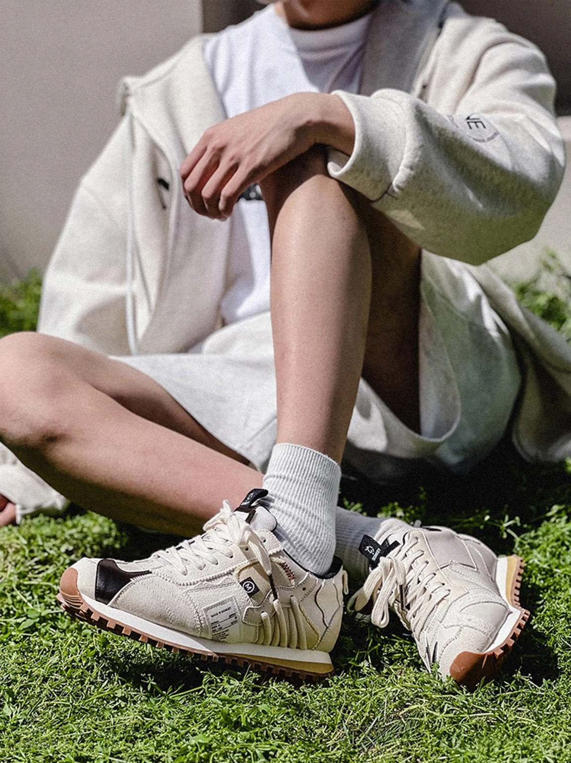 Ivory waffle sole retro sneakers styled with neutral casual streetwear beside a seated model near a grassy roadside