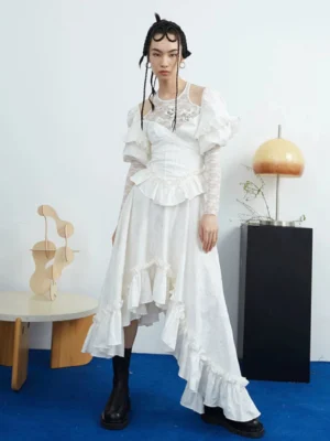 Full body ivory white asymmetric ruffle midi dress with long sheer lace sleeves, gathered waist and floor grazing layered ruffle hem styled with black boots