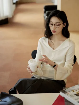 Ivory white women's collared knit sweater with button front, elegant relaxed slim fit, and softly flared long sleeves styled in a modern office lounge