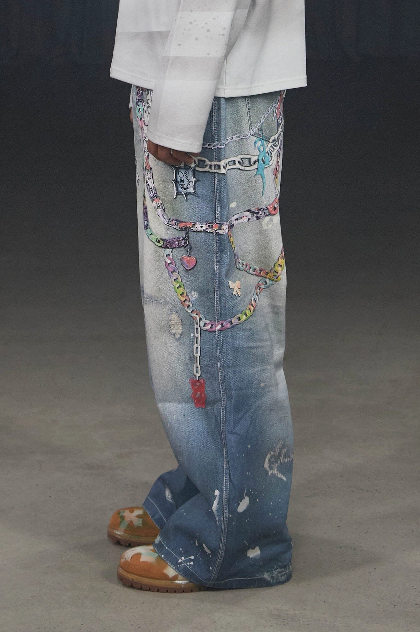 Close side view of blue washed Kawaii chain jeans showing colorful heart charms distressed fading and paint-splatter streetwear details