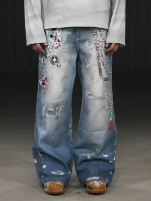Front low-angle view of light blue Kawaii chain wide-leg jeans with colorful cartoon graphics distressed patches and paint-splatter streetwear details