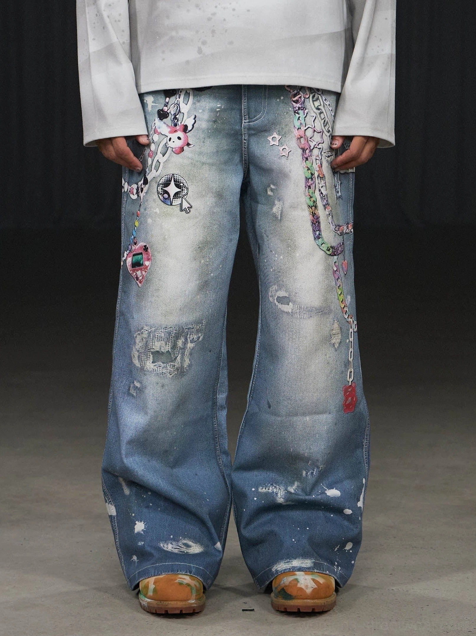 Front low-angle view of light blue Kawaii chain wide-leg jeans with colorful cartoon graphics distressed patches and paint-splatter streetwear details