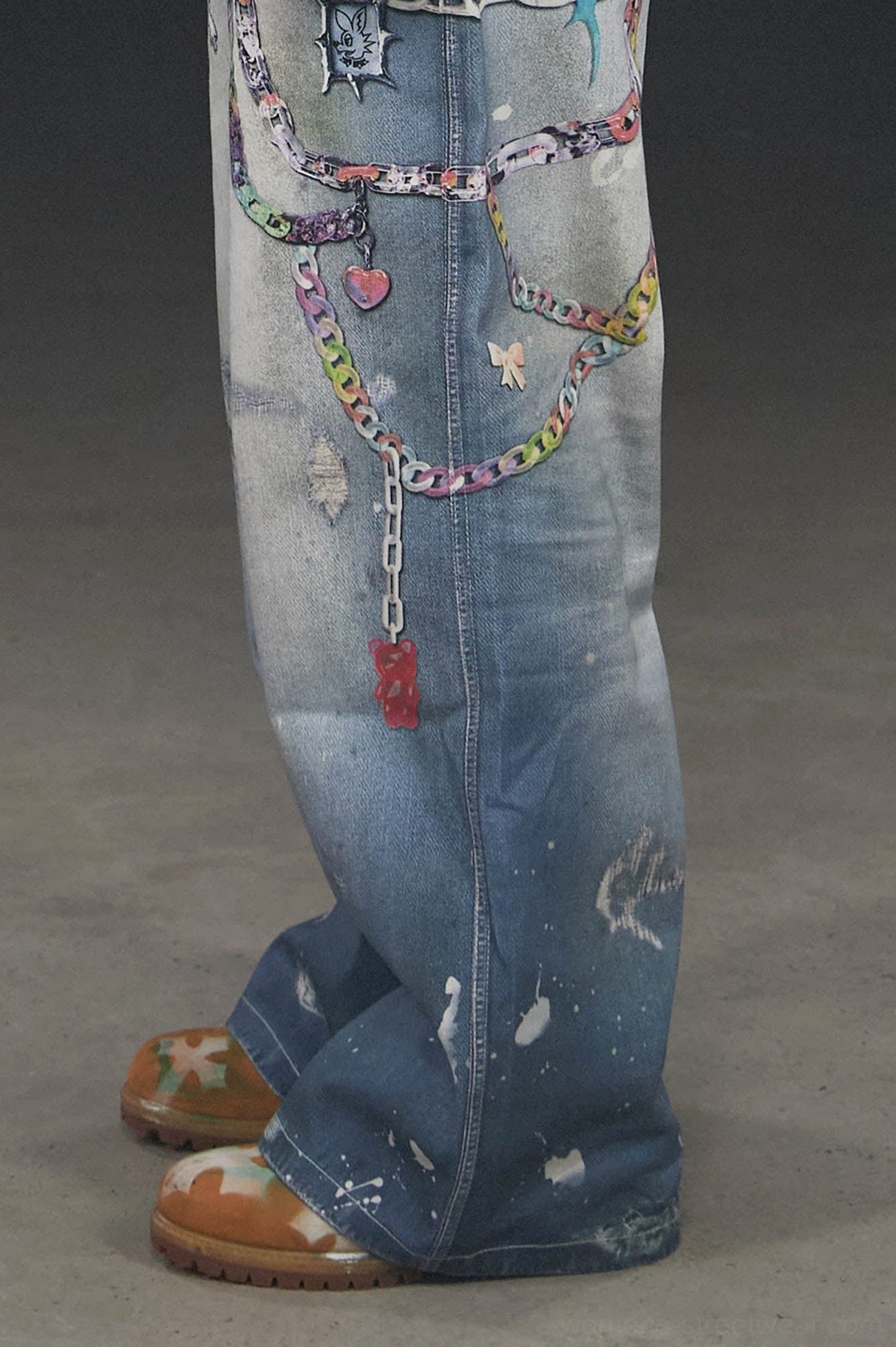 Close-up of Kawaii graphic wide-leg jeans showing colorful chain prints heart and tag charms worn edges and washed blue denim