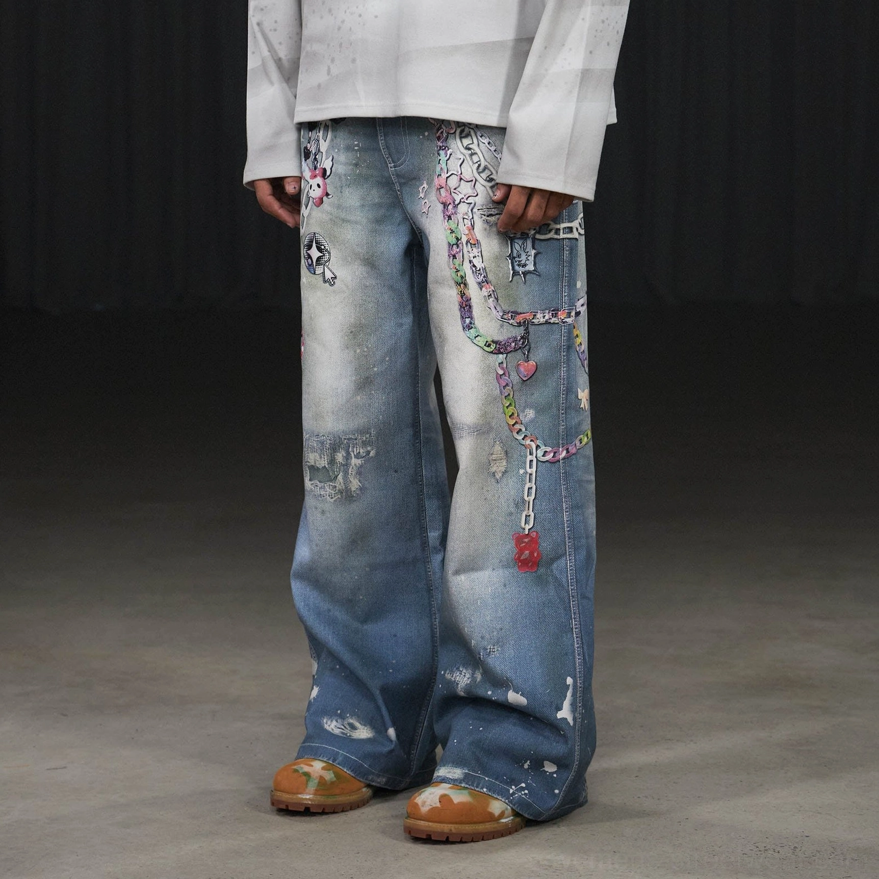 Three-quarter side view of light-wash Kawaii graphic wide-leg jeans with colorful chain prints heart charms star motifs and paint splatters