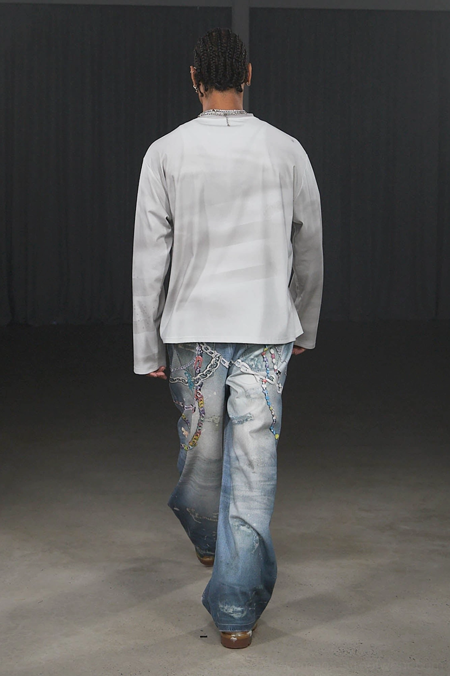 Full rear walking view of male model wearing faded blue Kawaii wide-leg jeans with rear chain details and relaxed urban styling