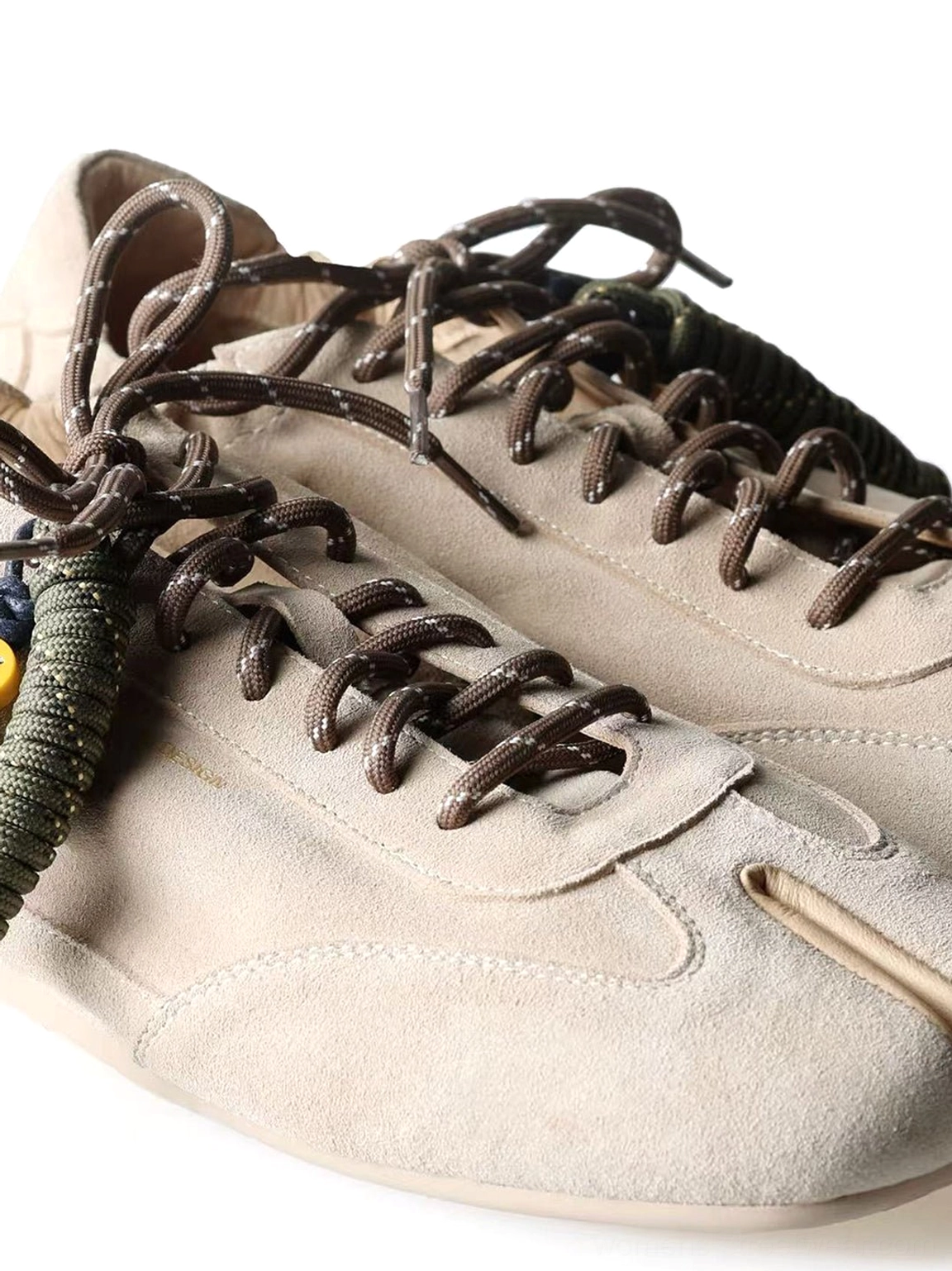 Close-up of khaki cowhide suede tabi sneakers showing split-toe construction and yellow black beaded laces