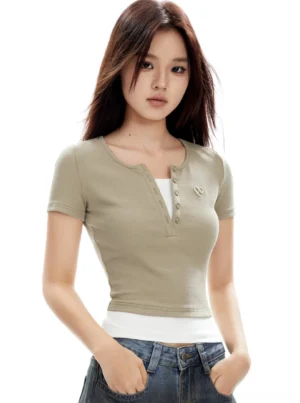 Front three-quarter view of a khaki cropped Henley short sleeve top with ribbed texture, button neckline, and heart chest embroidery