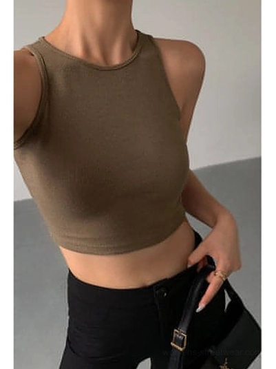 Khaki cropped ribbed knitted tank top front close-up upper body shot - ribbed knit texture with crew neck and sleeveless cropped fit paired with black pants and black leather handbag on plain indoor background