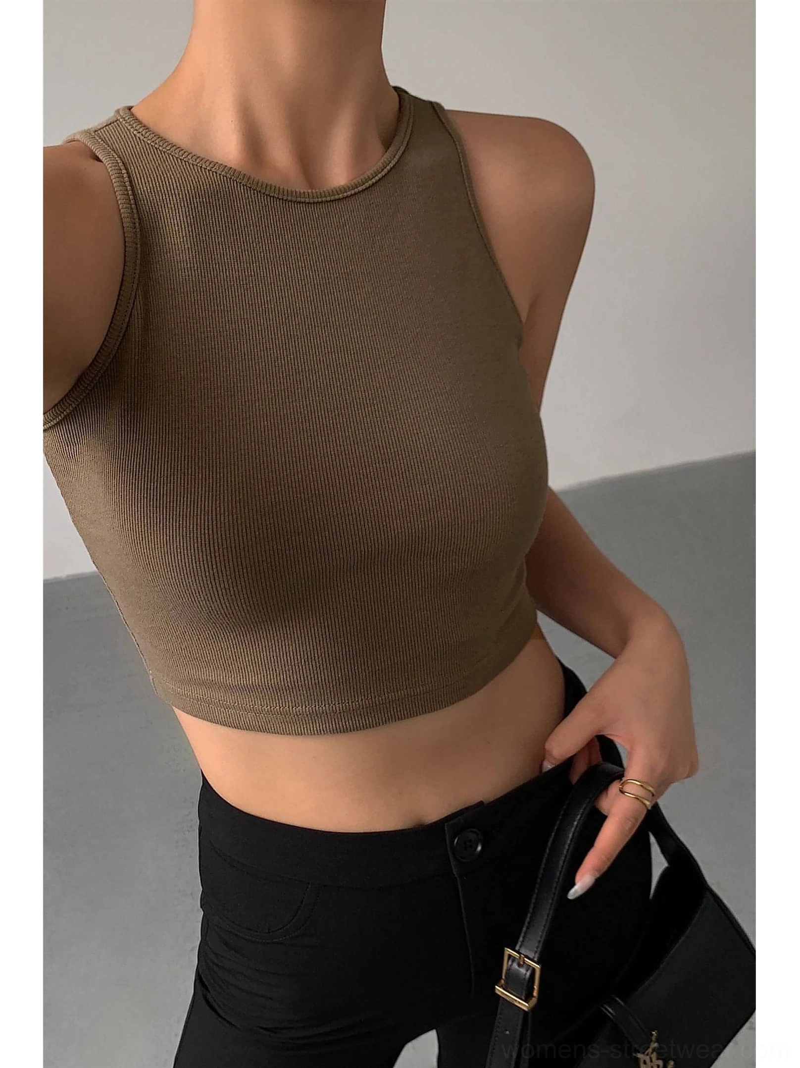 Khaki cropped ribbed knitted tank top front close-up upper body shot - ribbed knit texture with crew neck and sleeveless cropped fit paired with black pants and black leather handbag on plain indoor background