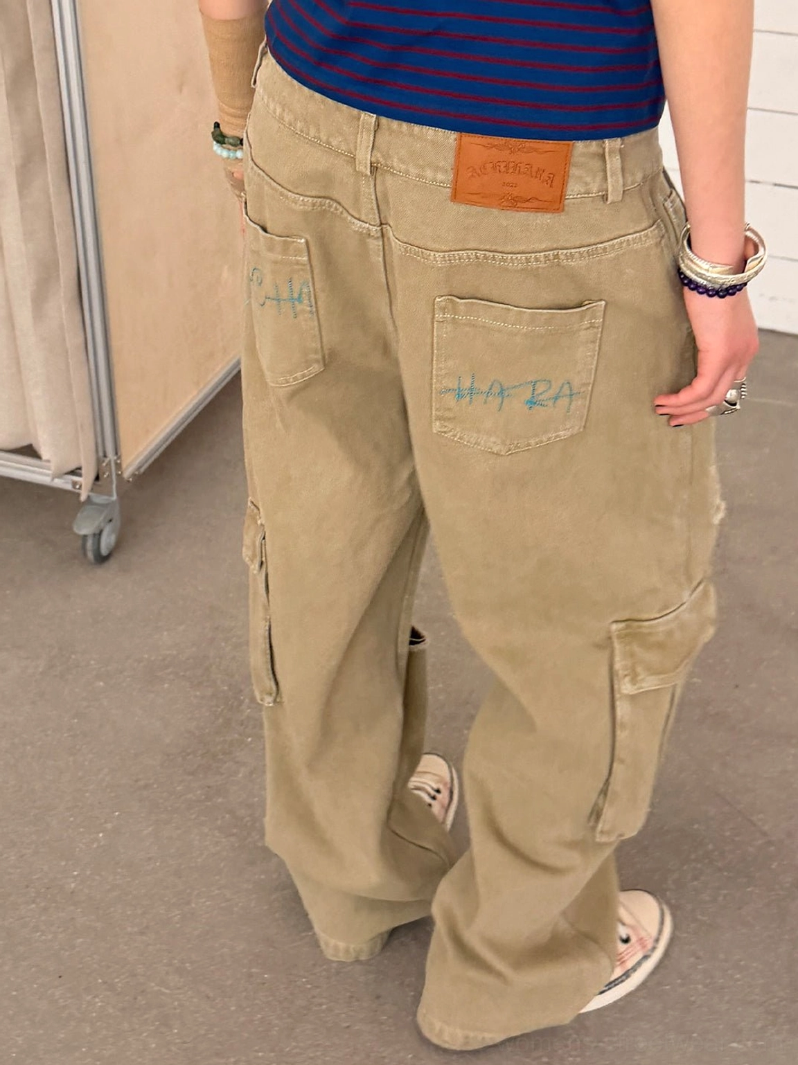 Rear view of khaki distressed cargo streetwear pants with waistband patch, graffiti-style back pockets, and wide-leg silhouette