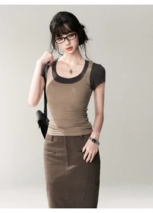 Front three-quarter view of a fitted khaki green and dark brown two-tone scoop neck streetwear top styled with a brown midi pencil skirt, black crossbody bag, necklace, and wristwatch