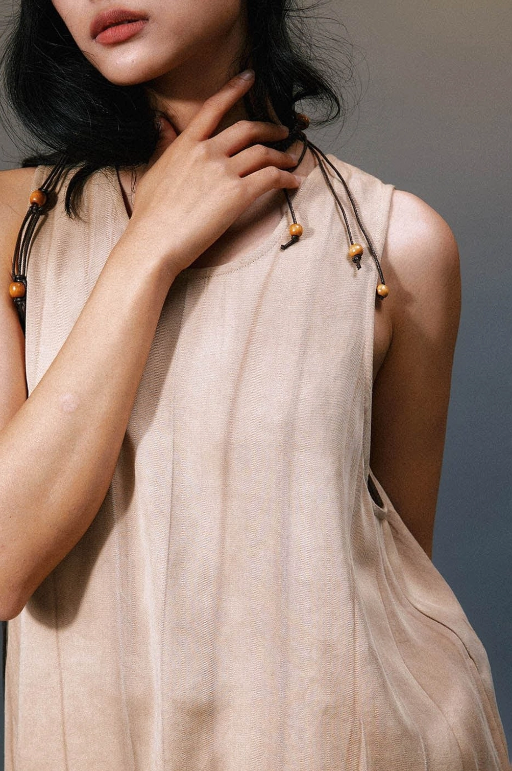 Close-up of soft khaki linen fabric and wooden beaded drawstring neck accessory on layered maxi dress