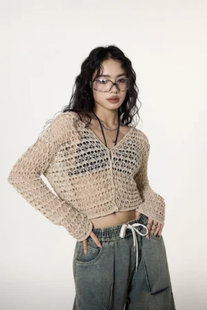 Back three-quarter view of a khaki open-knit crochet crop cardigan styled with relaxed washed cargo denim