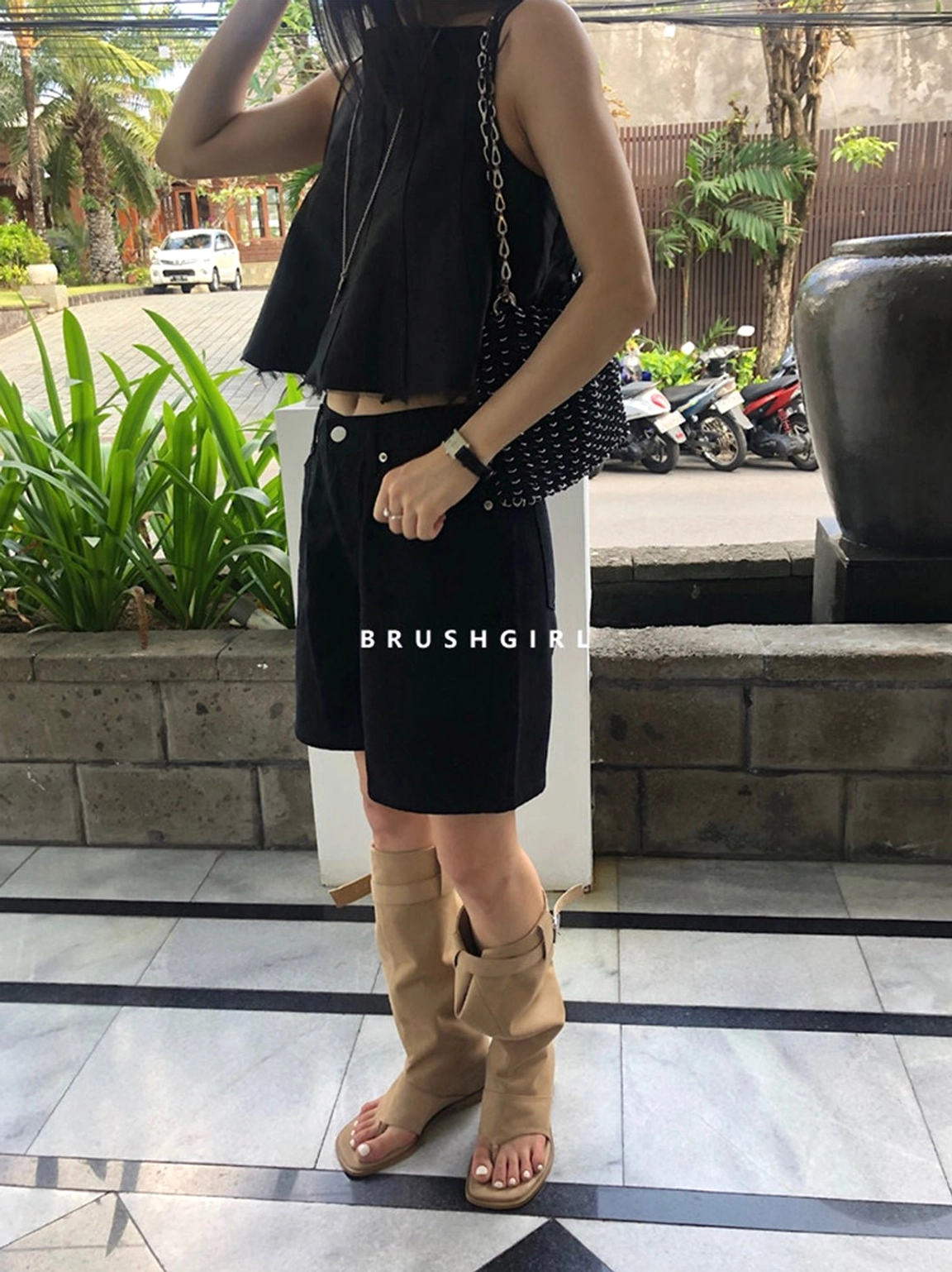 Front three-quarter styling of khaki open-toe knee-high sandal boots with black shorts and a crossbody bag