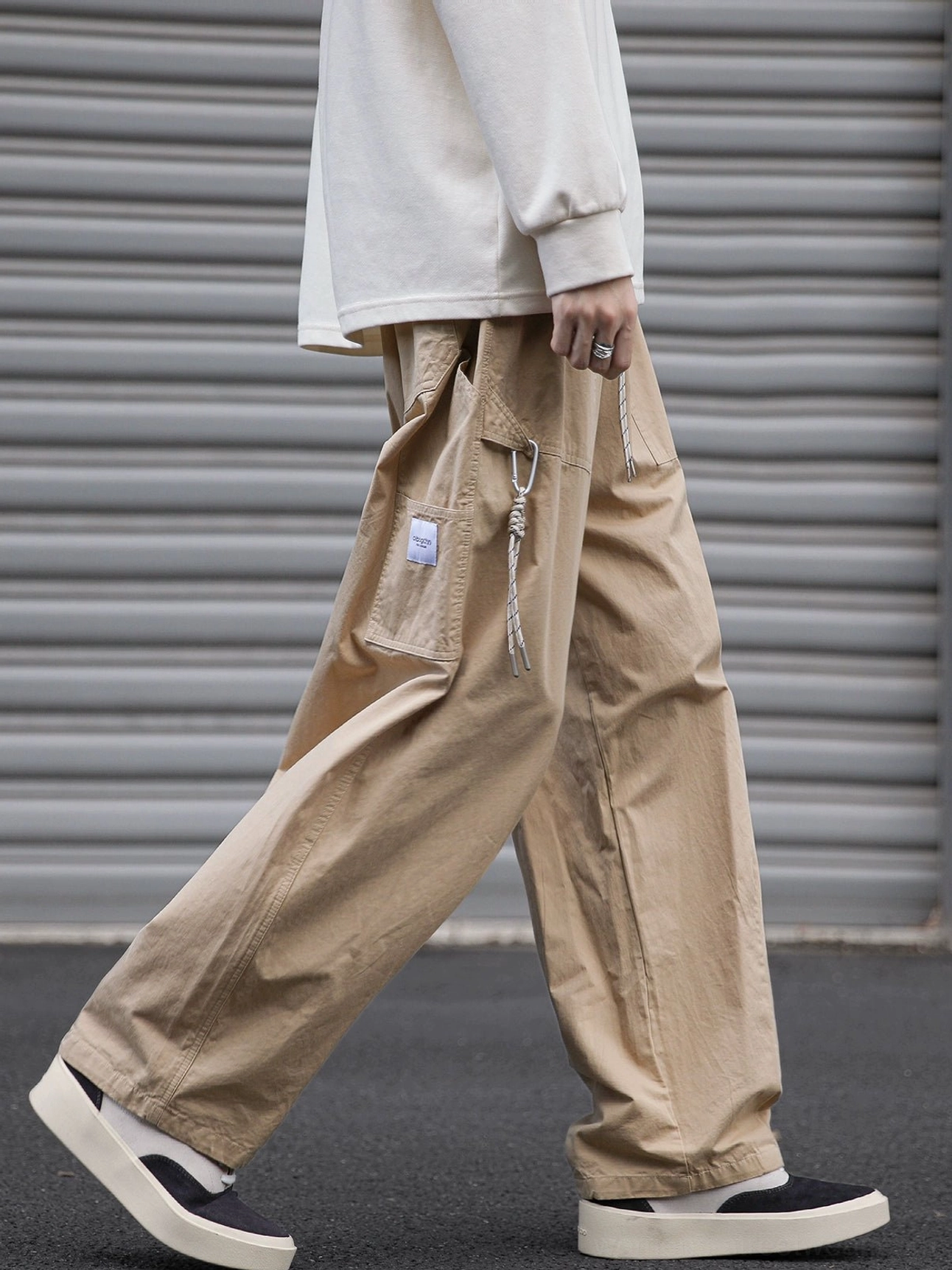 Khaki relaxed utility cargo pants shown in motion with oversized side cargo pocket, drawstring detail, straight wide-leg fit, cream top, and casual skate shoes