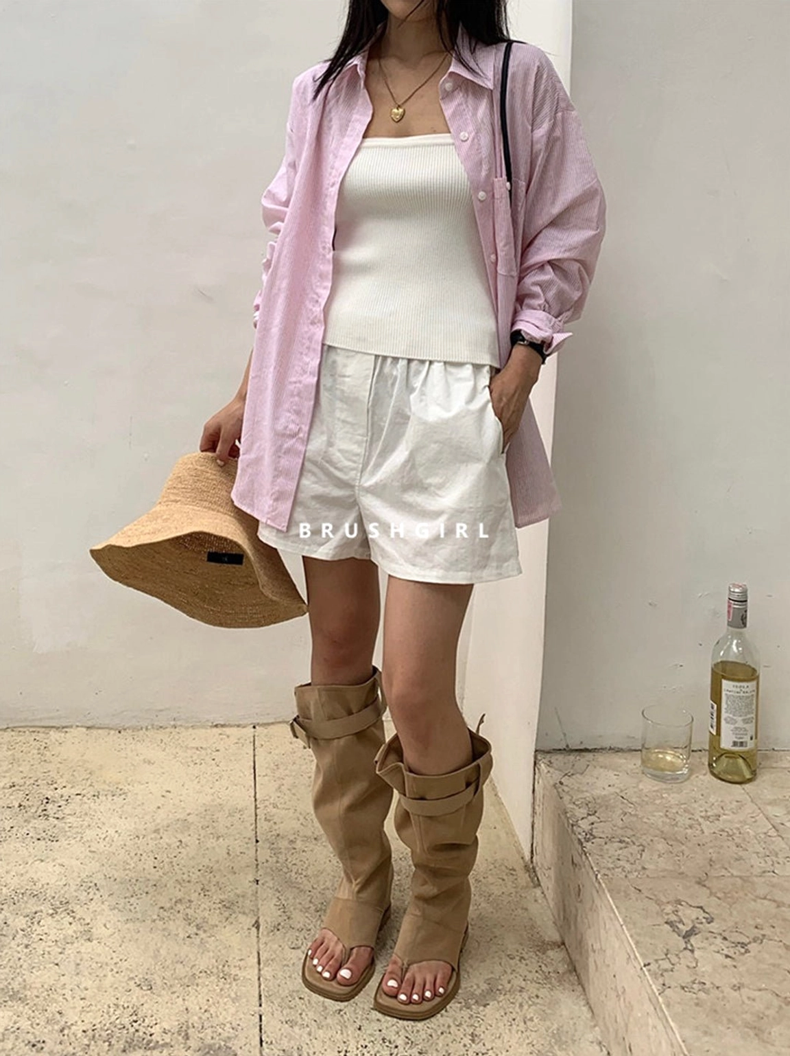 Three-quarter view of a model styling khaki slouchy thong knee-high boots with white shorts and a pink shirt