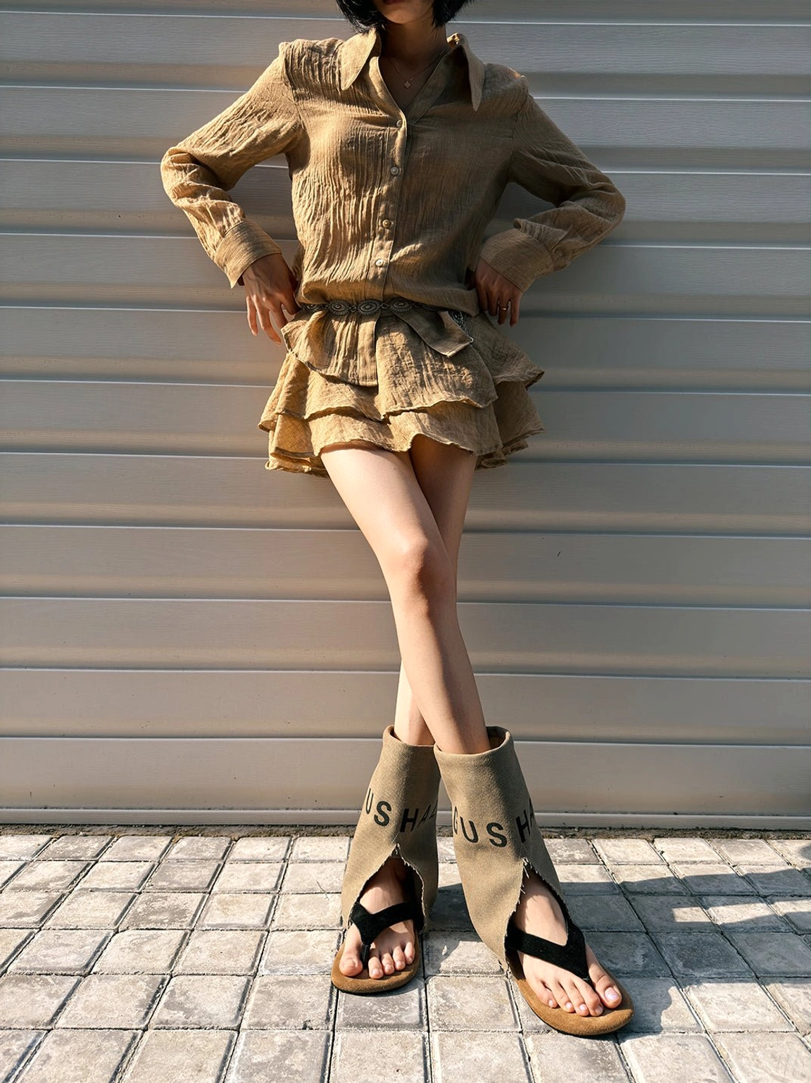 Front view of khaki split-toe mid-calf sandal boots styled with a linen two-piece outfit and contemporary urban fashion