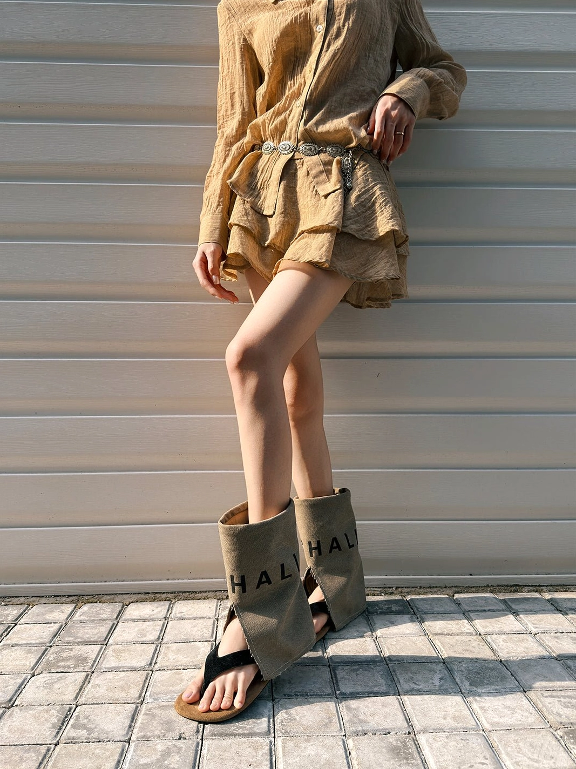 Model wearing khaki split-toe western sandal boots with graphic printed shaft and tan suede footbed in a casual streetwear outfit