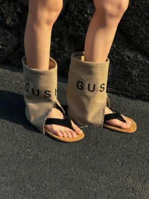 Model wearing khaki split-toe western sandal boots with relaxed mid-calf shaft, open thong toe, and printed streetwear lettering