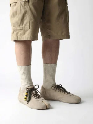 Model wearing khaki suede tabi sneakers with cargo shorts and beige socks in a minimalist streetwear outfit