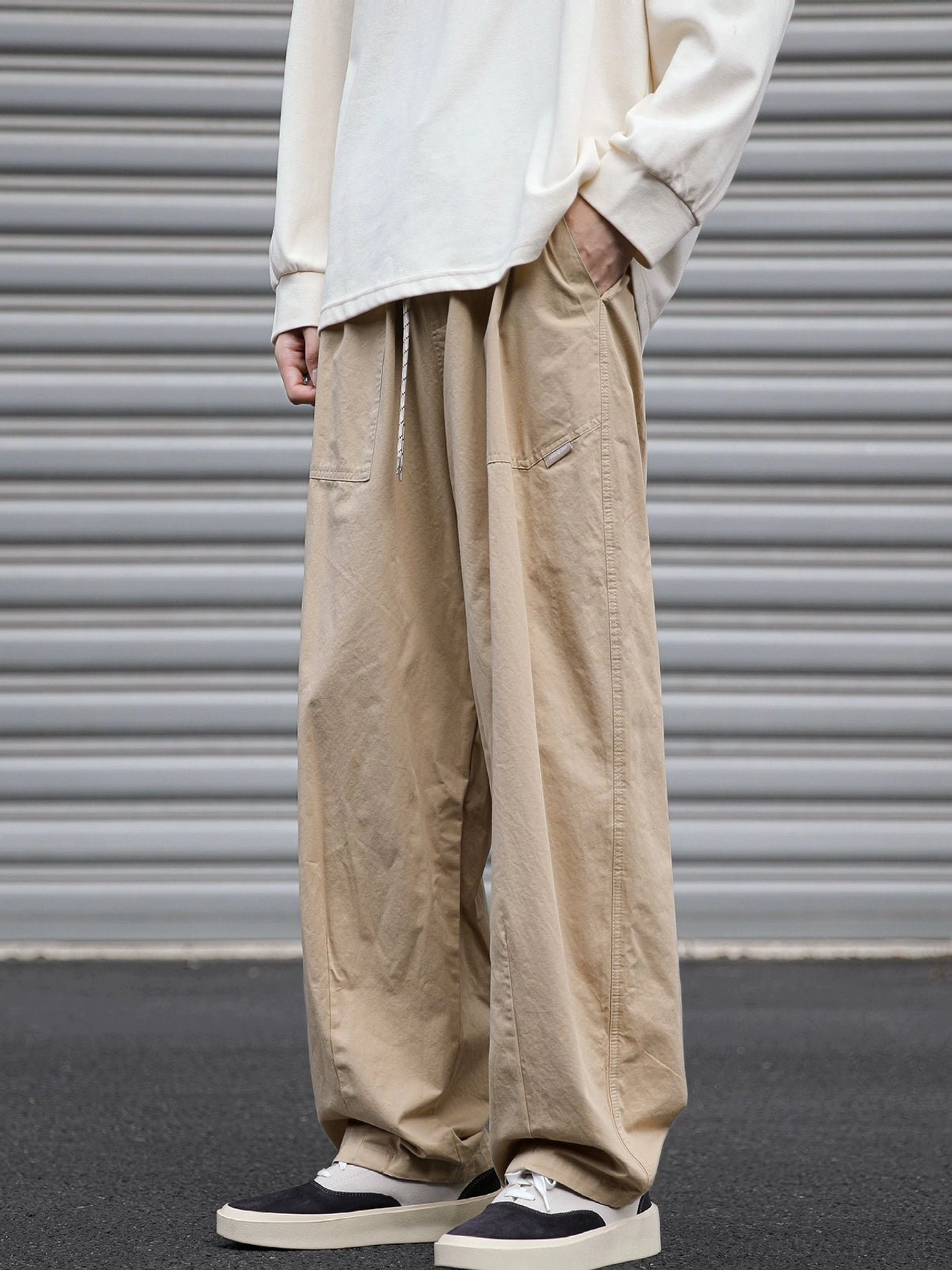 Khaki utility cargo pants shown from the front side with drawstring waist, clean solid twill design, relaxed straight-leg profile, cream shirt, and low-top sneakers