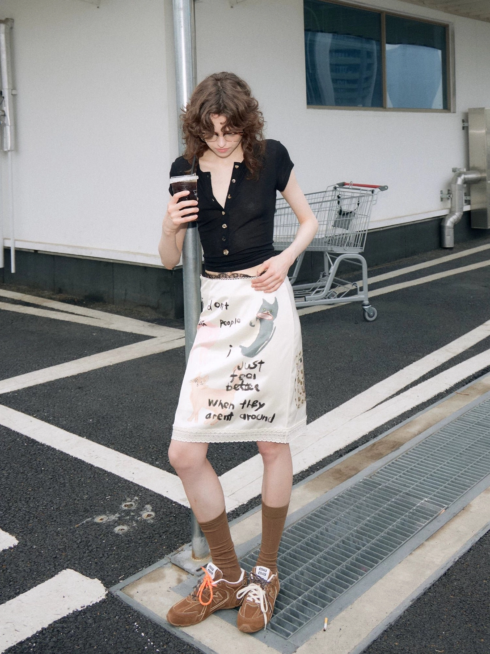 Full outfit view of an apricot kitty slogan print midi pencil skirt styled with a black top and sneakers for everyday streetwear