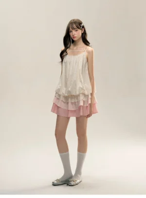 Three-quarter front view of Korean-inspired cream embroidered mini slip dress with pink layered ruffle skirt, square neckline, white socks, and silver loafers
