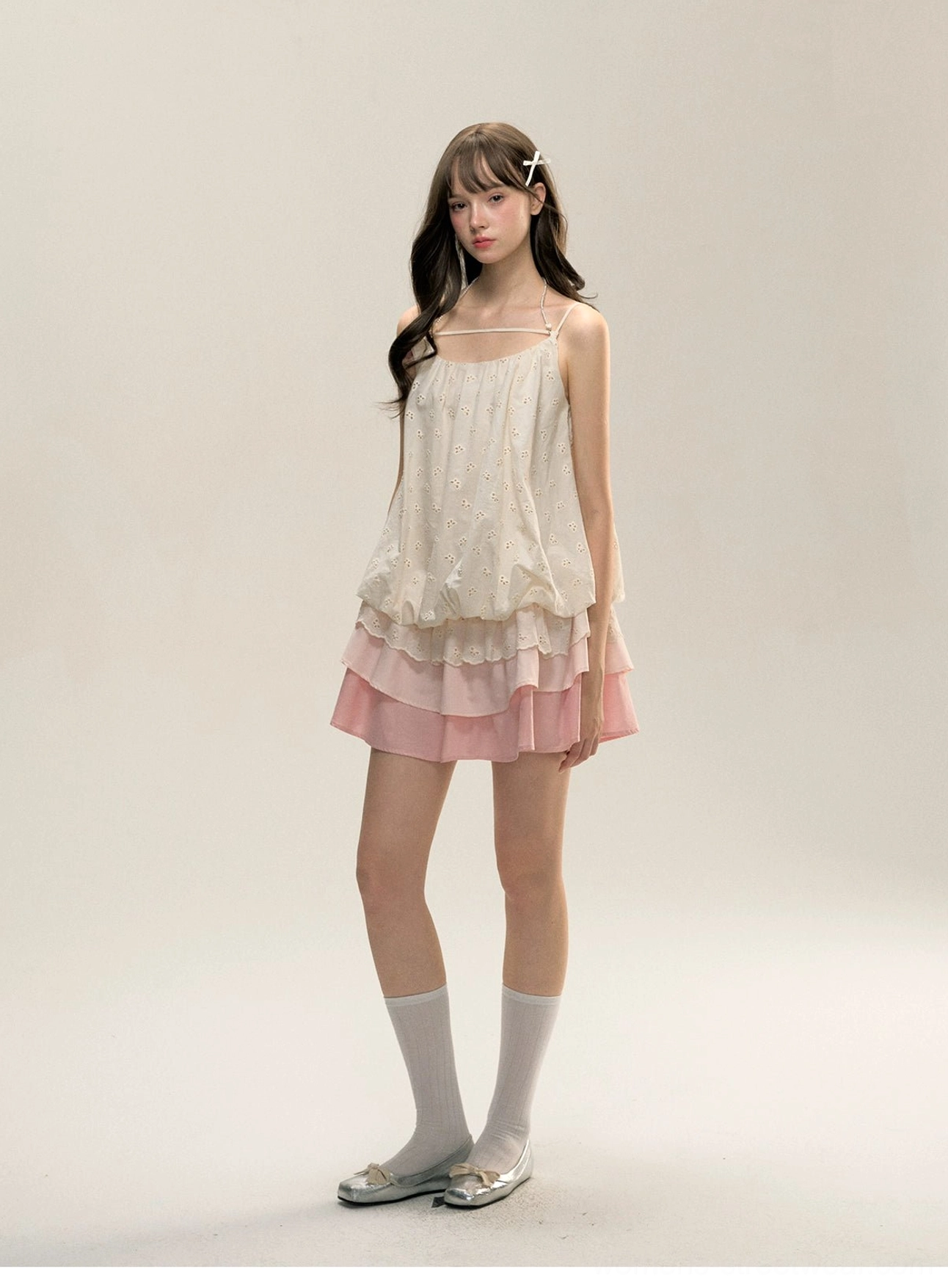 Three-quarter front view of Korean-inspired cream embroidered mini slip dress with pink layered ruffle skirt, square neckline, white socks, and silver loafers