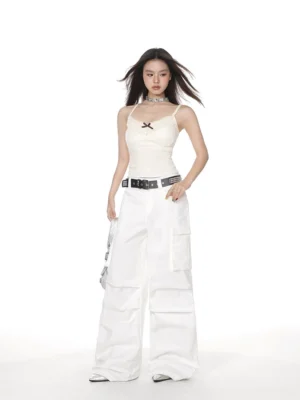 White lace trim camisole tank top with slim fit V-neck, black bow detail, and spaghetti straps styled with wide-leg cargo pants