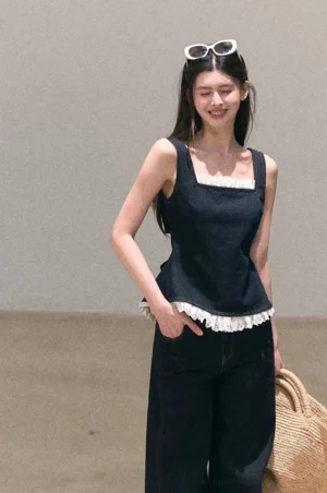 Front view of a dark wash lace trim denim peplum cami top with square neckline and white eyelet lace hem