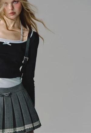 Close-up of lace-trim pleated grey skirt with tiny waist bow detail and layered black white cropped tops - preppy streetwear styling