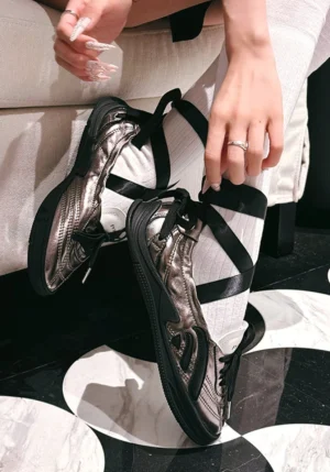 Silver and black ribbon lace cutout ballet sandals worn on feet in an indoor streetwear styling look