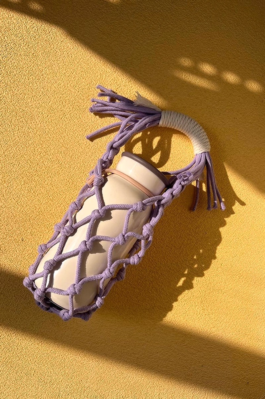 Lavender lilac cotton macrame water bottle carrier with tumbler, shown from an angled view with secure knotted net structure