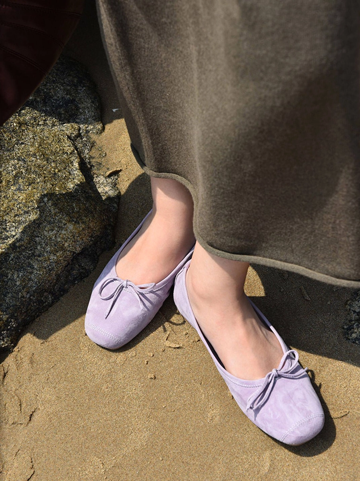 Model wearing lavender square-toe bow ballet flats with a dark brown long skirt outdoors