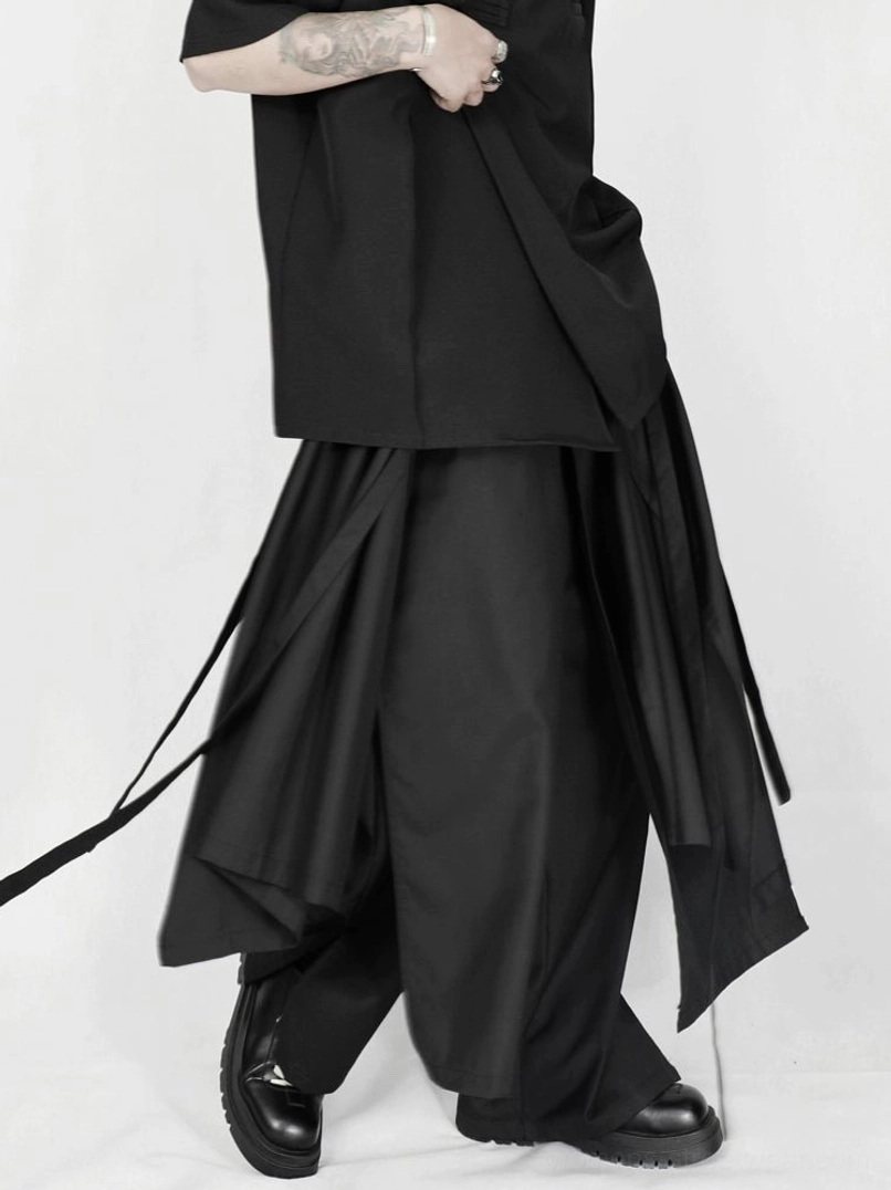 Side view of layered asymmetric draped black trousers with floor-length wide-leg silhouette